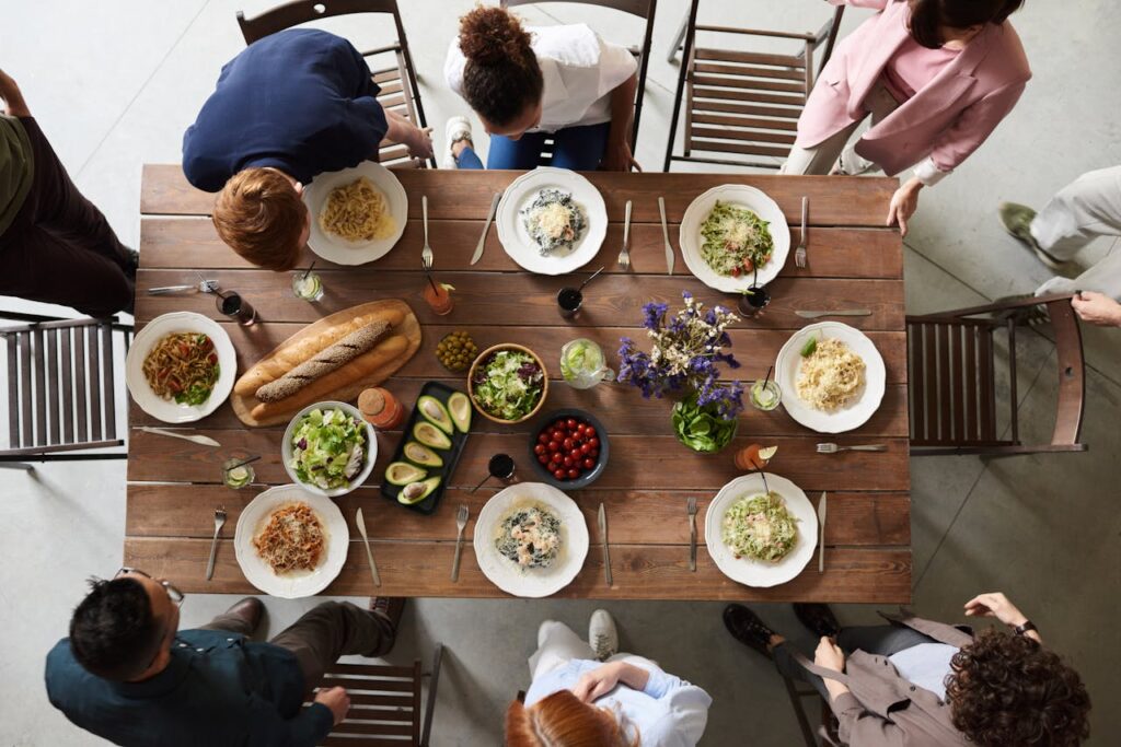 A diverse group of people sharing a meal around a wooden table, viewed from above.