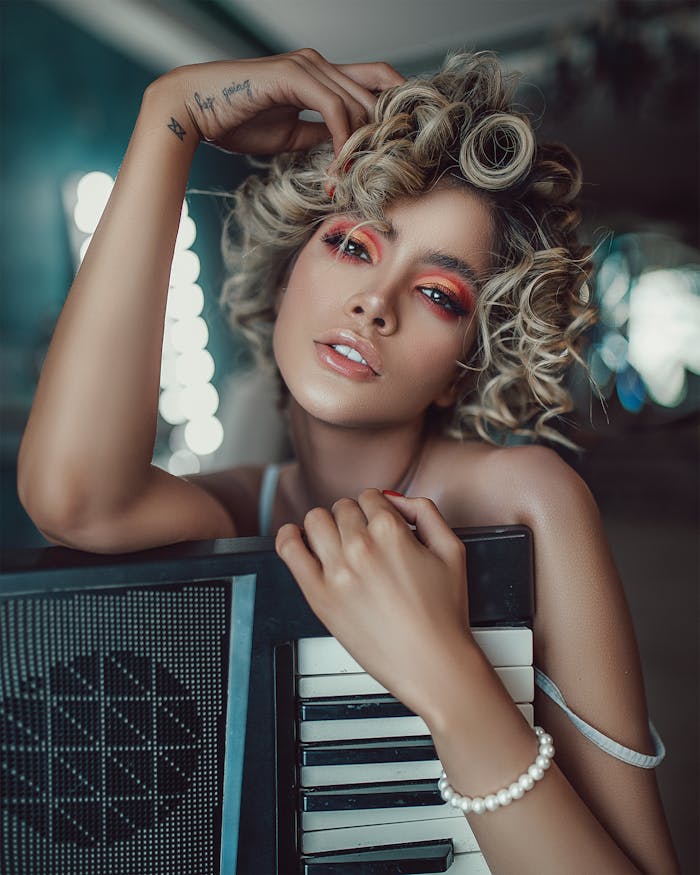 Self assured young female singer with curly hair and makeup standing in modern studio with synthesizer before concert